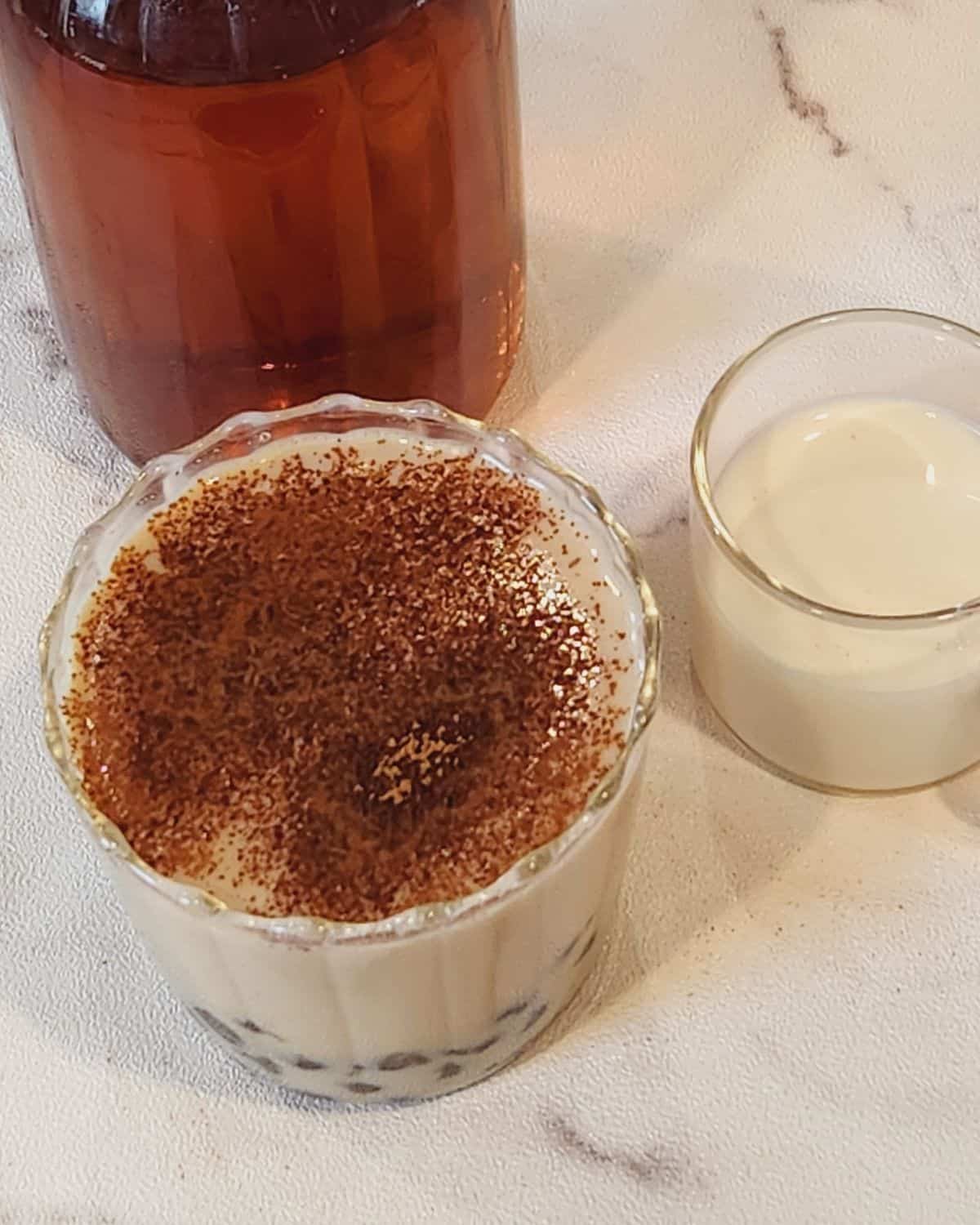 A glass of oolong milk tea with additional milk next to it.