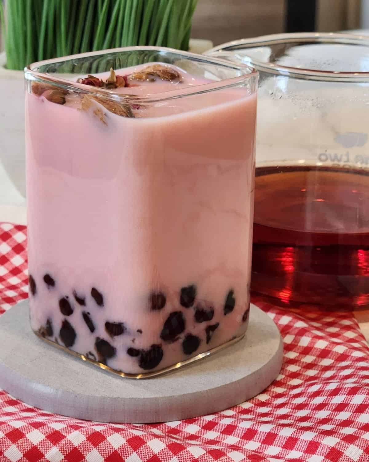 A glass of Rose milk tea with boba or tapioca pearls.