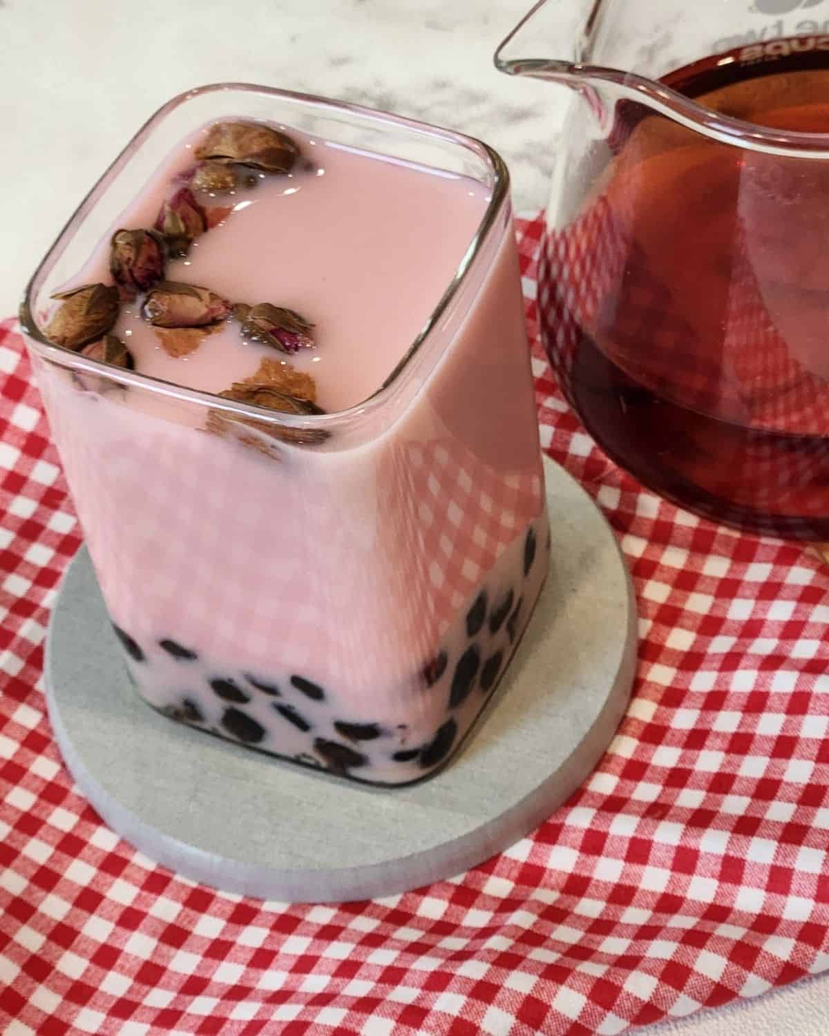 A glass of Rose milk tea with boba or tapioca pearls.