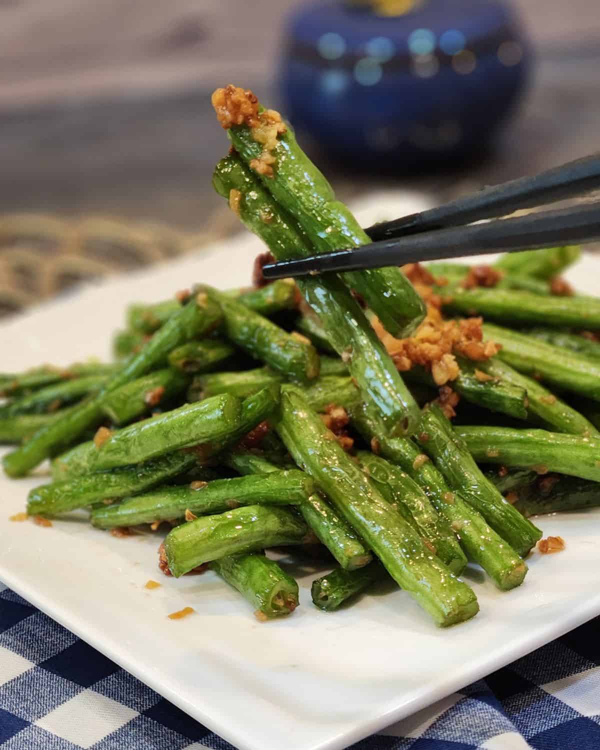 A pair of chopsticks holding the sautéed green beans with garlic.