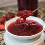 A spoon scooping fresh strawbery compote from a small plate.