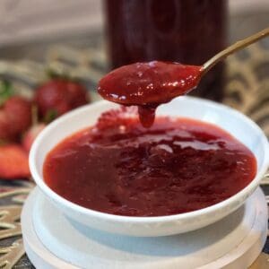 A spoon scooping fresh strawbery compote from a small plate.