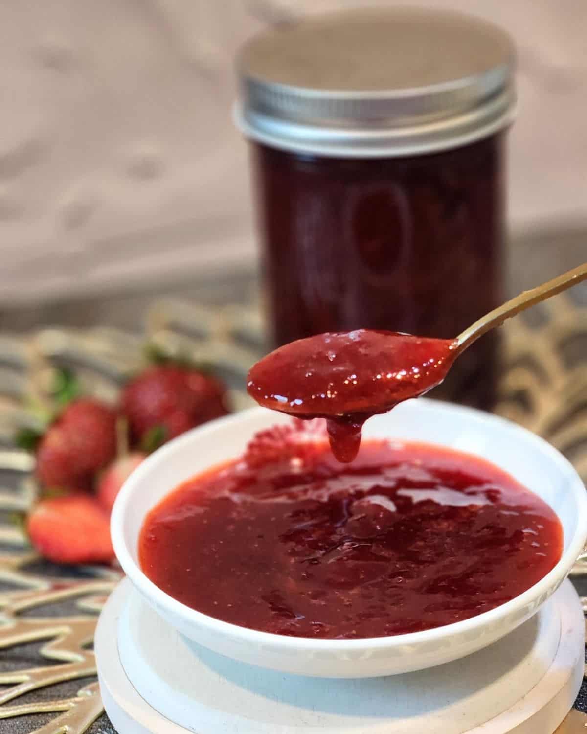 A spoon scooping fresh strawbery compote from a small plate.