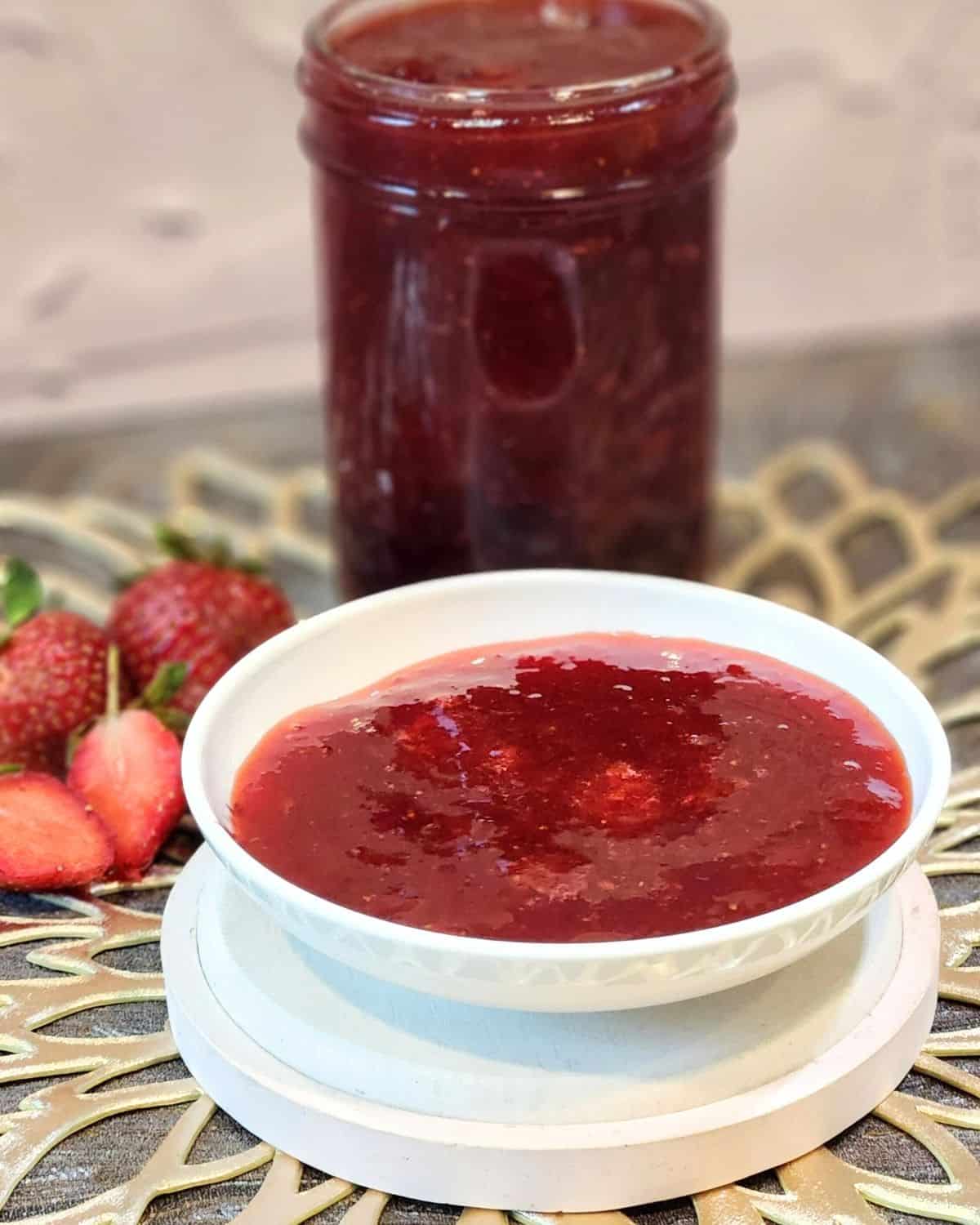 A small plate of strawberry compote with a jar full of it behind.