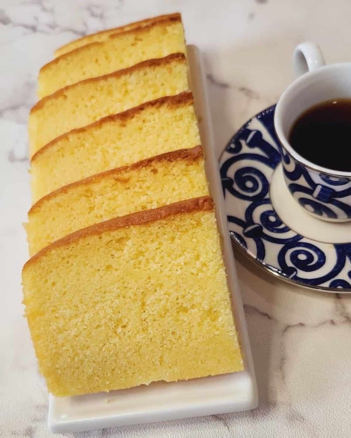 A photo of Thai butter cake slices on a white plate next to a cup of coffee.