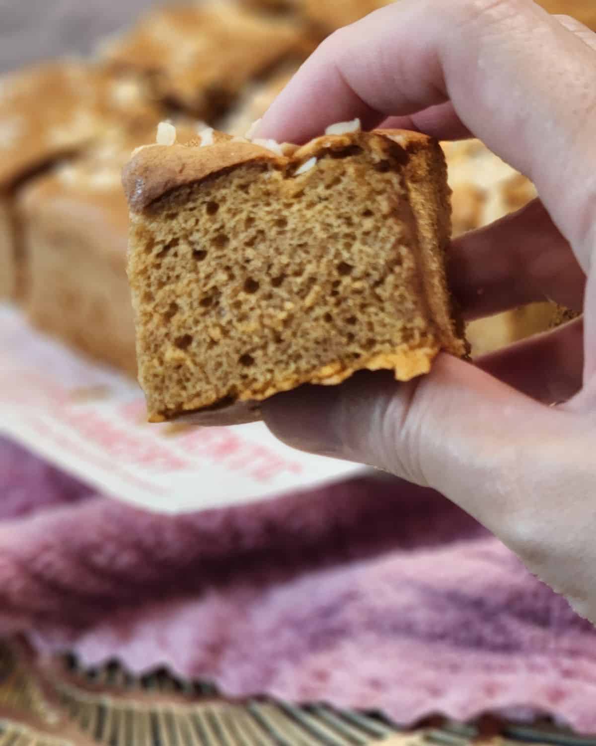 A hand holding a slice of Dutch ontbijtkoek cake, showing the fluffy texture.