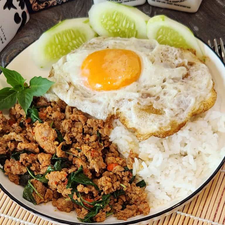 Pad Kra Pao pork dish with crispy fried egg, holy basil, and fresh cucumber slices.