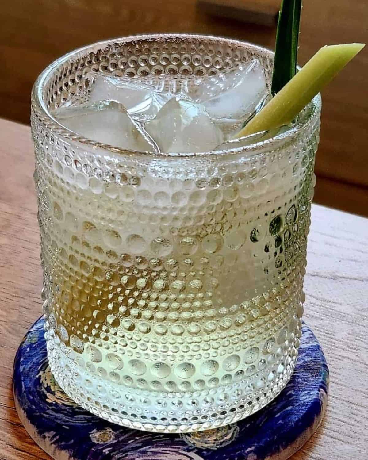 A glass of lemongrass pandan tea with pandan leaf and lemongrass stalk for decoration.