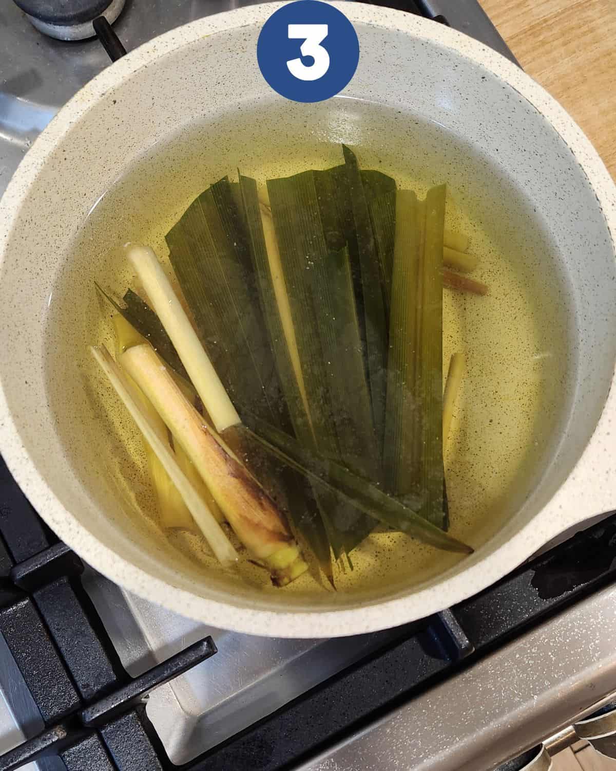 Simmering water in a pot with pandan leaves and lemongrass stalks.