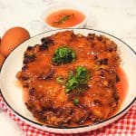A plate of two pork and shrimp egg foo young patties with tomato sauce drizzled on top and scallions for garnish.