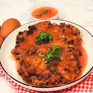 A plate of two pork and shrimp egg foo young patties with tomato sauce drizzled on top and scallions for garnish.