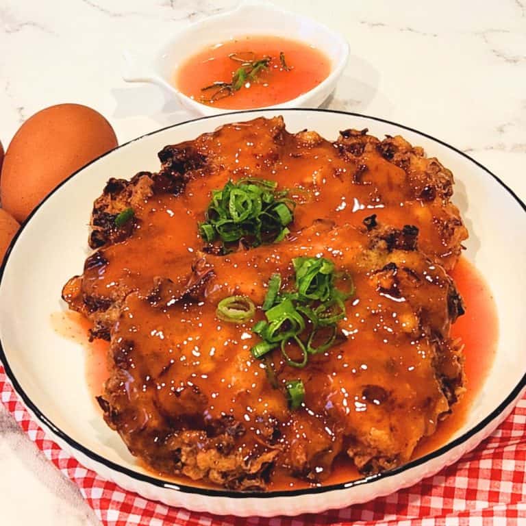A plate of two pork and shrimp egg foo young patties with tomato sauce drizzled on top and scallions for garnish.