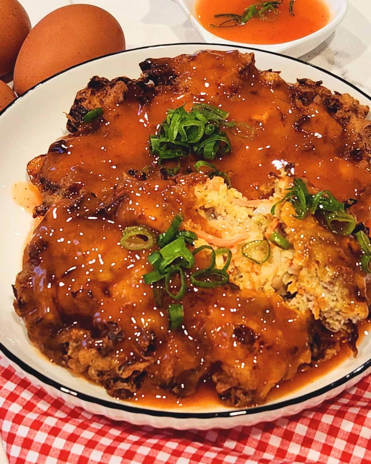 A plate of two pork and shrimp egg foo young patties with tomato sauce drizzled on top and scallions for garnish.