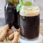 A glass of Tamarind tea with fresh mint leaves decoration.