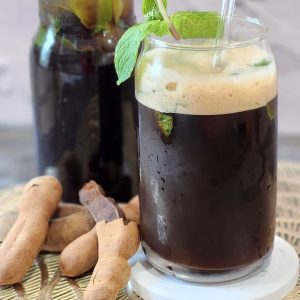 A glass of Tamarind tea with fresh mint leaves decoration.