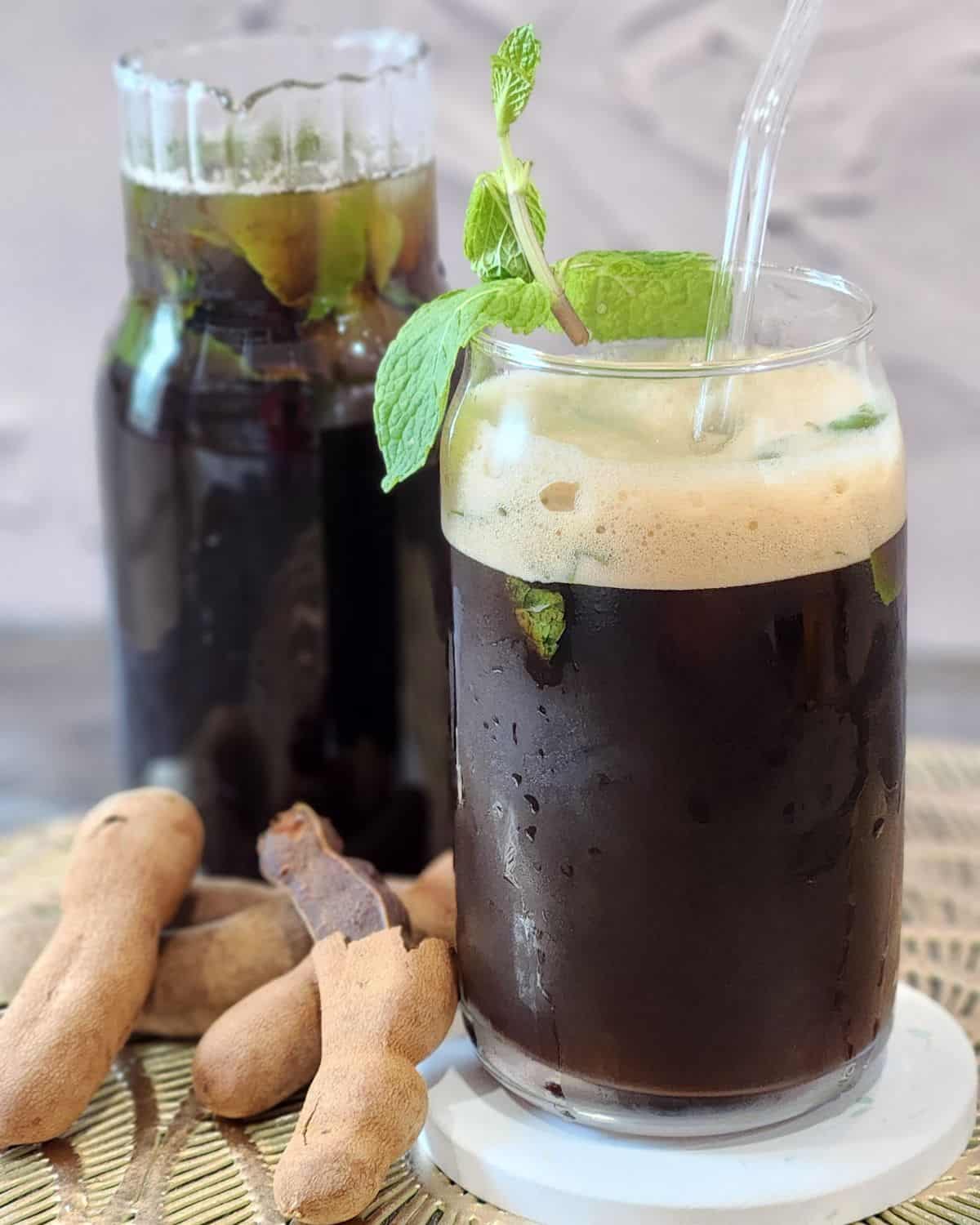 A glass of frothed tamarind tea with some fresh mint leaves.