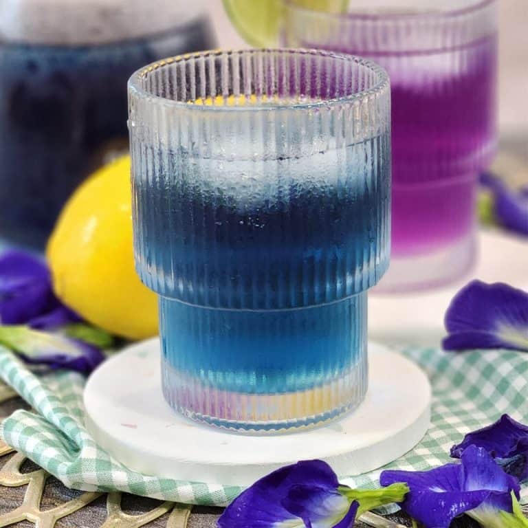 A glass of cold butterfly pea tea with ice cubes.
