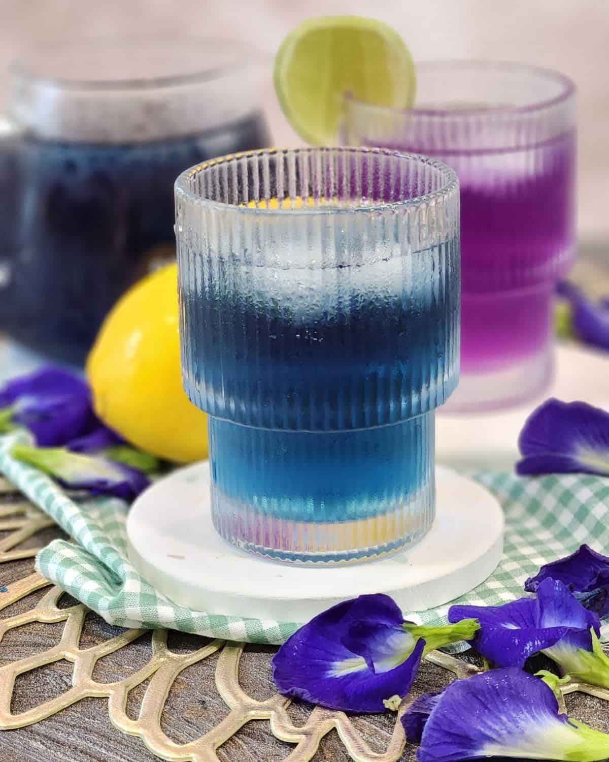 A glass of blue butterfly pea tea with some ice cubes in it.