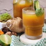 A glass of iced turmeric ginger tea with mint leaves as decoration and a wedge of lime.