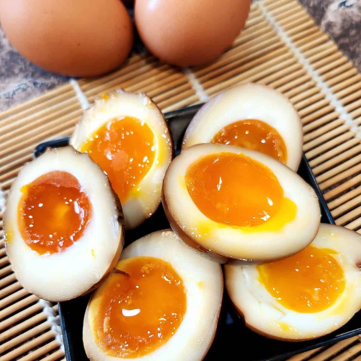 Ajitama or Ajitsuke tamago (ramen eggs) on a black plate and wooden tray.
