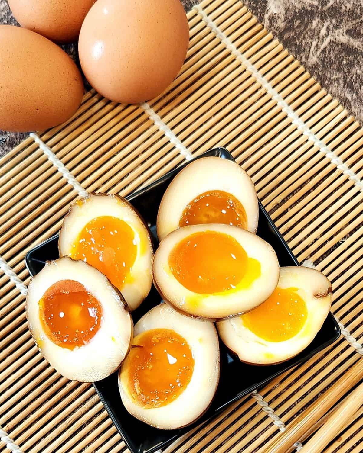 Ajitsuka tamago or ramen eggs cut in halves on bamboo tray.