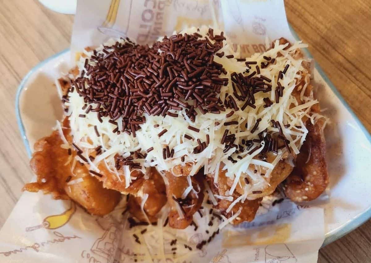 Indonesian banana fritters or pisang goreng drizzled with condensed milk, grated cheese, and chocolate rice.