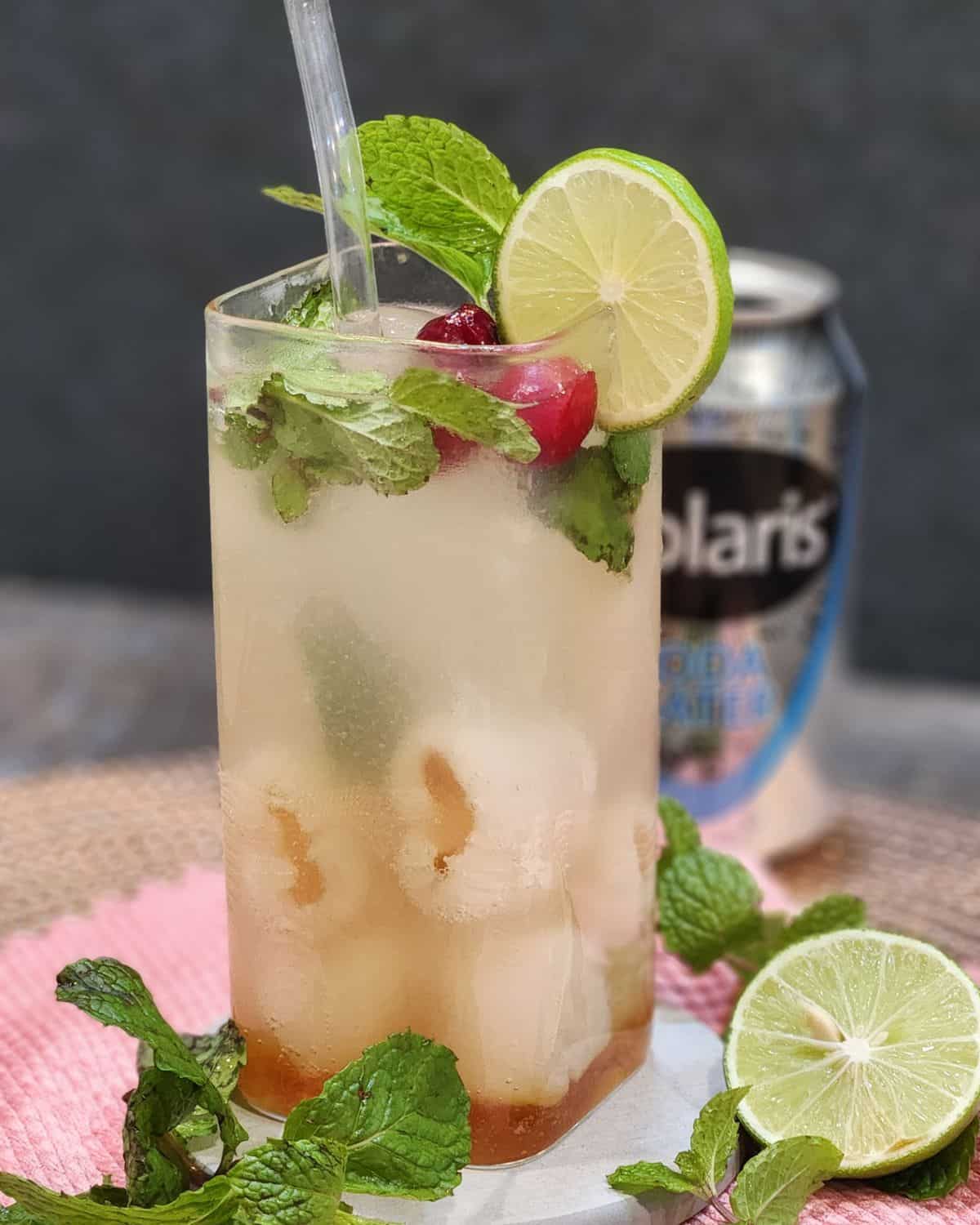 A tall glass of lychee soda garnished with mint leaves and lime slices.