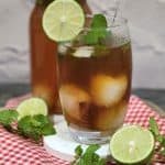 A glass of lychee tea garnished with mint leaves and lime slices.