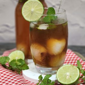 A glass of lychee tea garnished with mint leaves and lime slices.