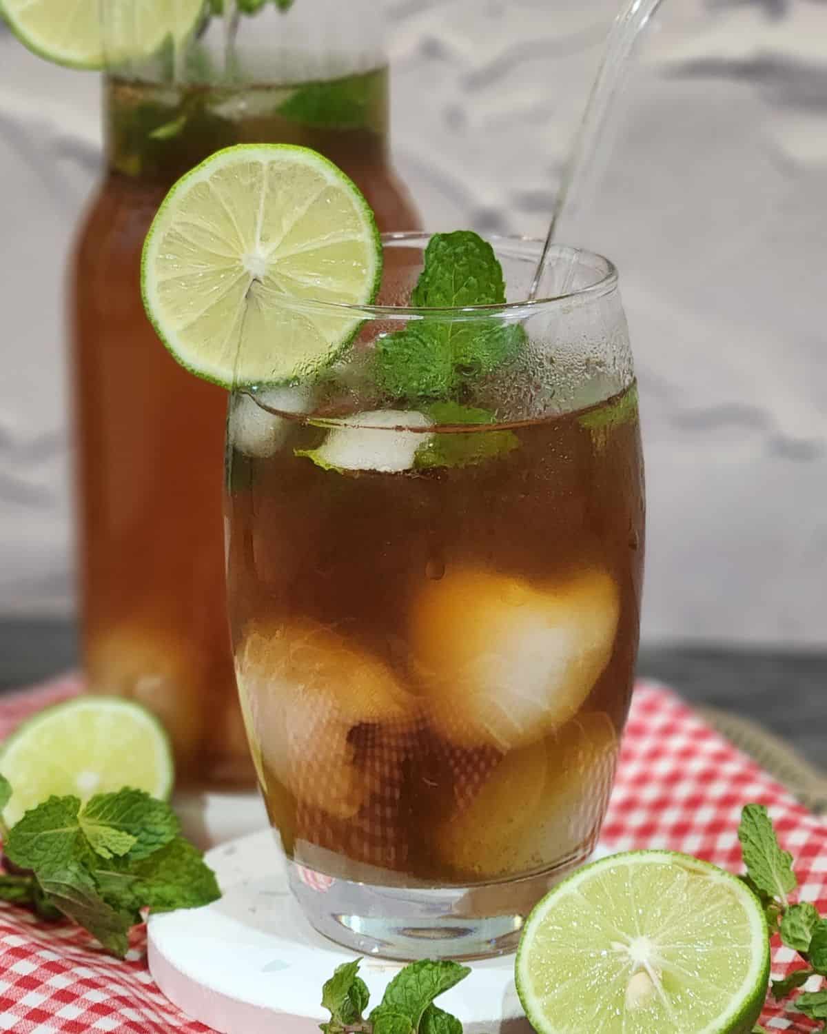 A glass of lychee tea garnished with mint leaves and lime slices.