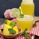 A glass of cold pineapple mint soda with some pineapple slices in front.