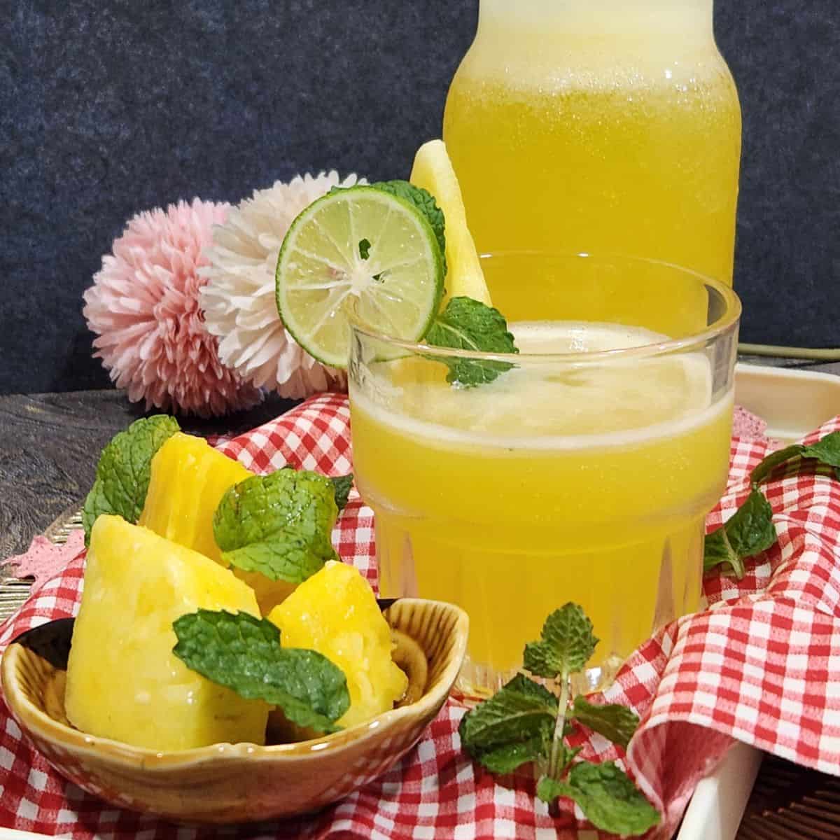 A glass of cold pineapple mint soda with some pineapple slices in front.