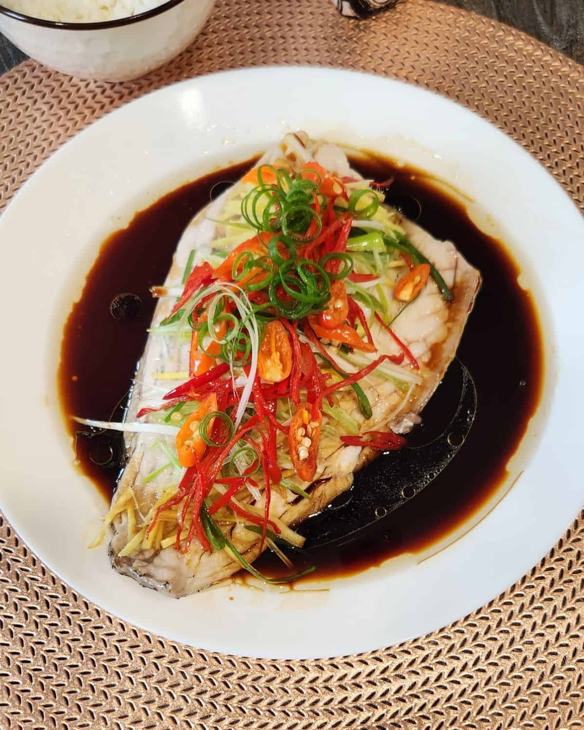 A plate of Cantonese steamed fish with ginger, chili, and scallions.