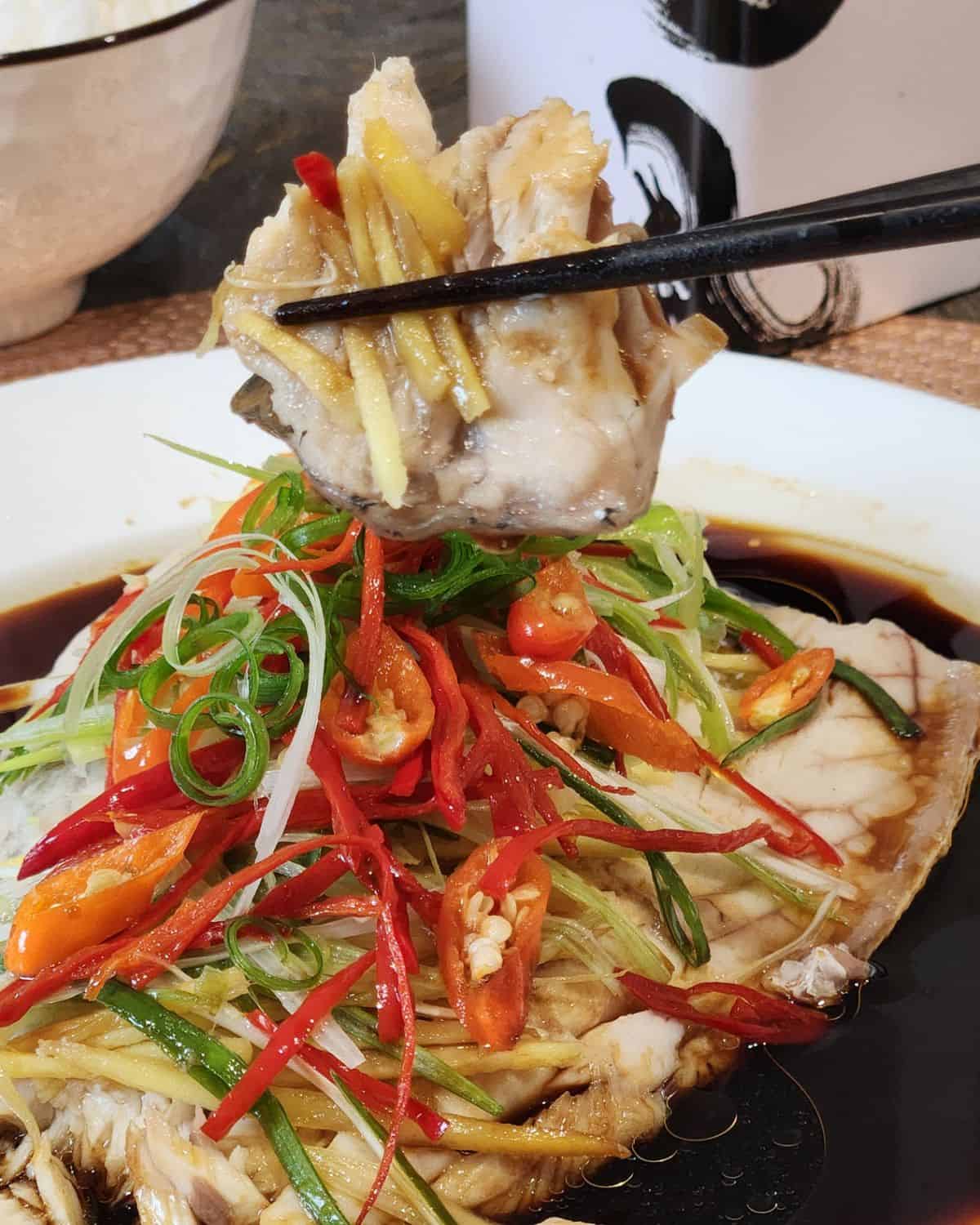 A pair of chopsticks holding a piece of Cantonese steamed fish.
