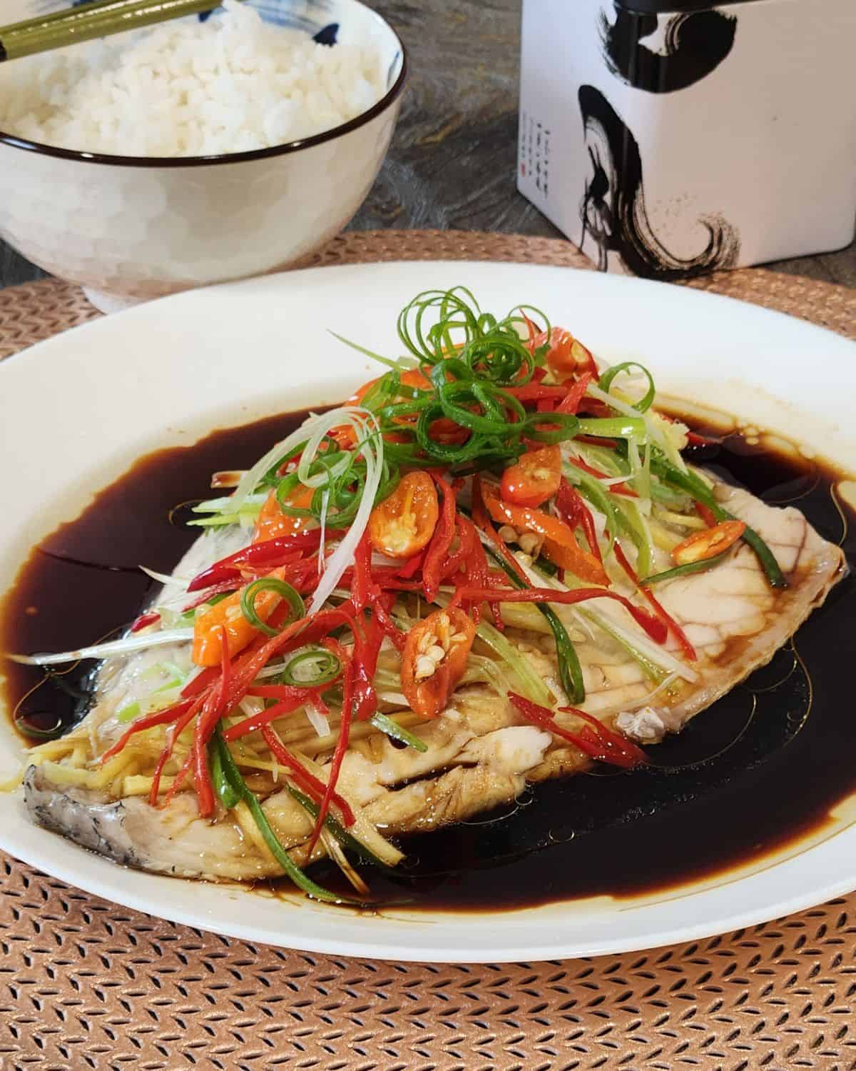 Cantonese steamed fish on a plate, garnished with ginger, scallion, and red chili.