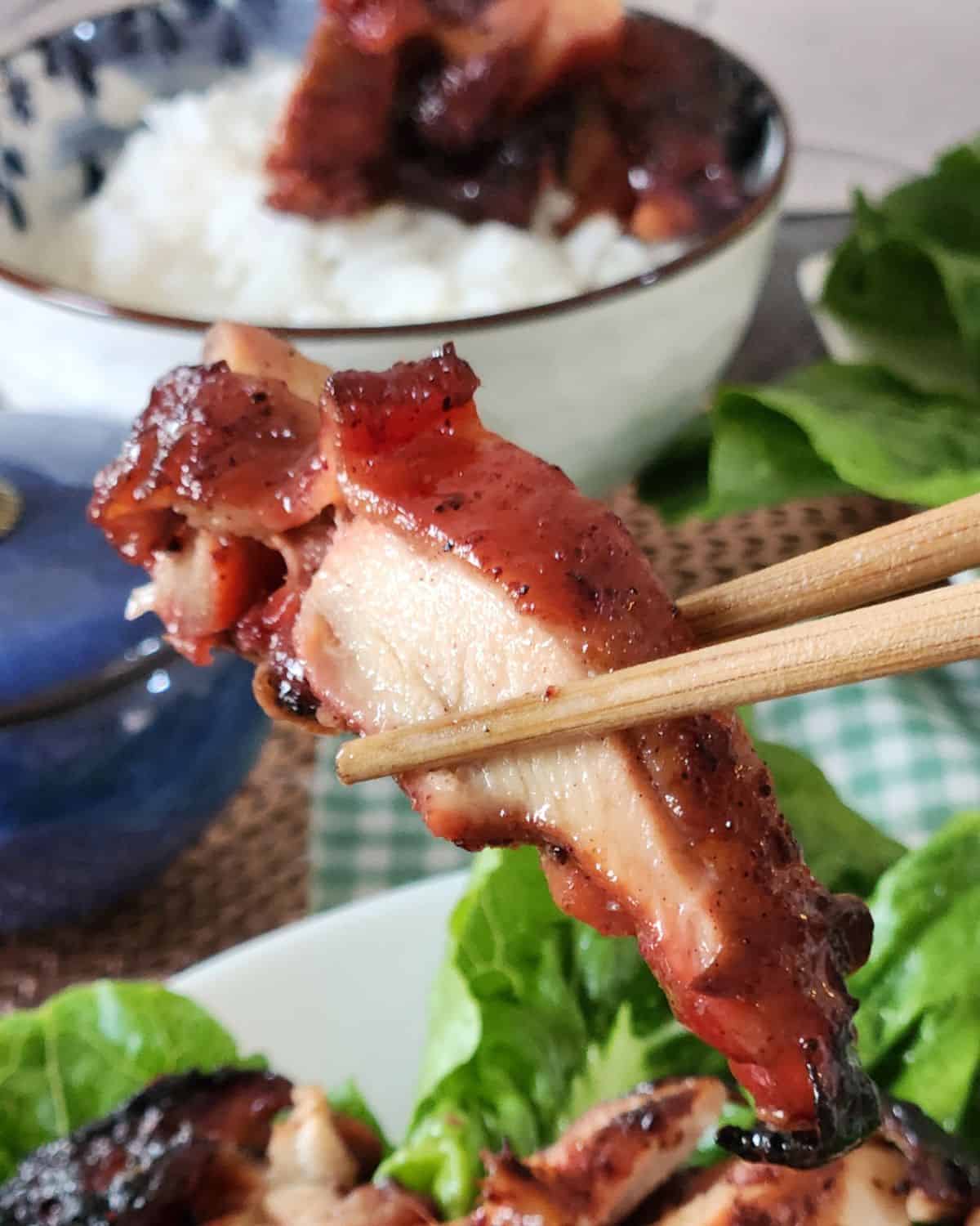 A pair of chopsticks holding char siu chicken piece.