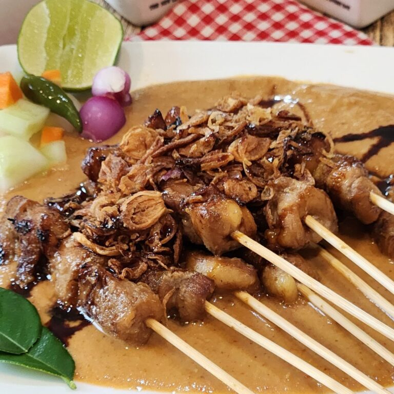 A plate of chicken satay with peanut sauce, pickles, and fried shallots.