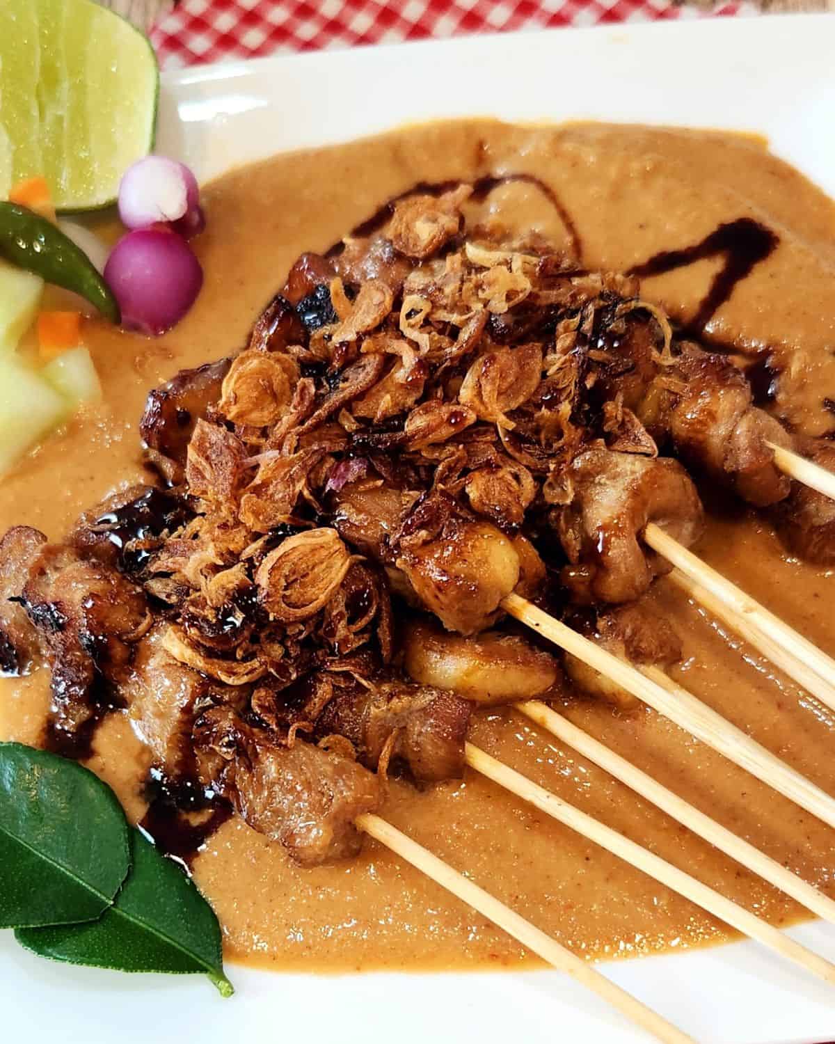 A plate of chicken satay with peanut sauce, pickles, and fried shallots.