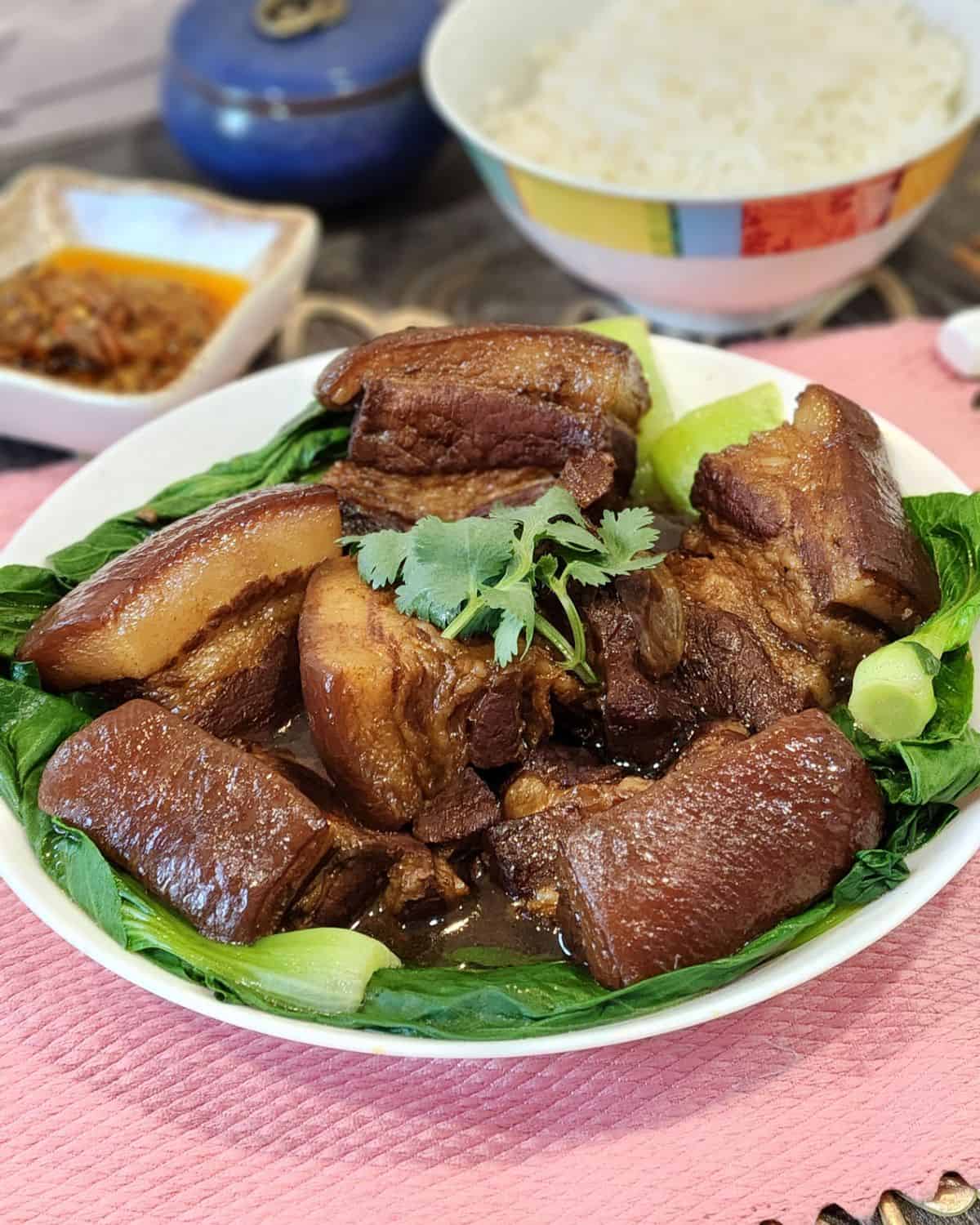 A big bowl of Chinese braised pork belly with blanched bok choy and steamed rice at the back.