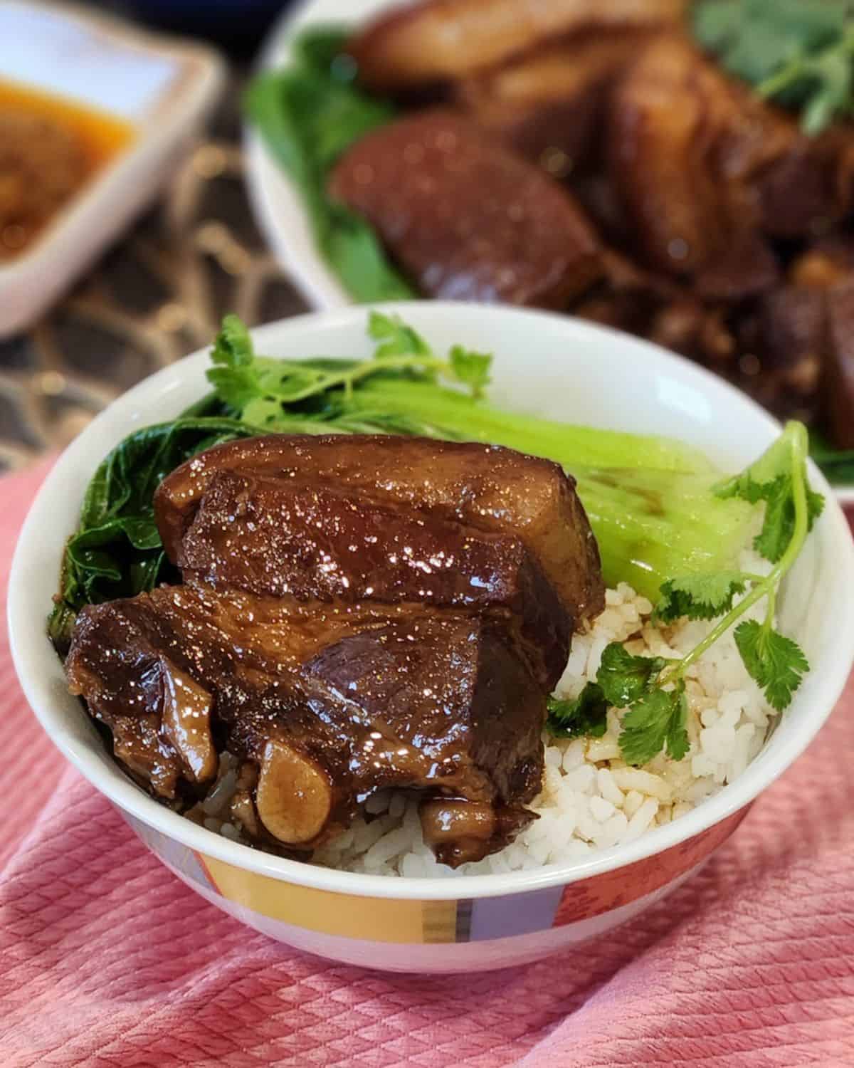 A bowl of steamed white rice with a piece of Chinese braised pork belly and bok choy.