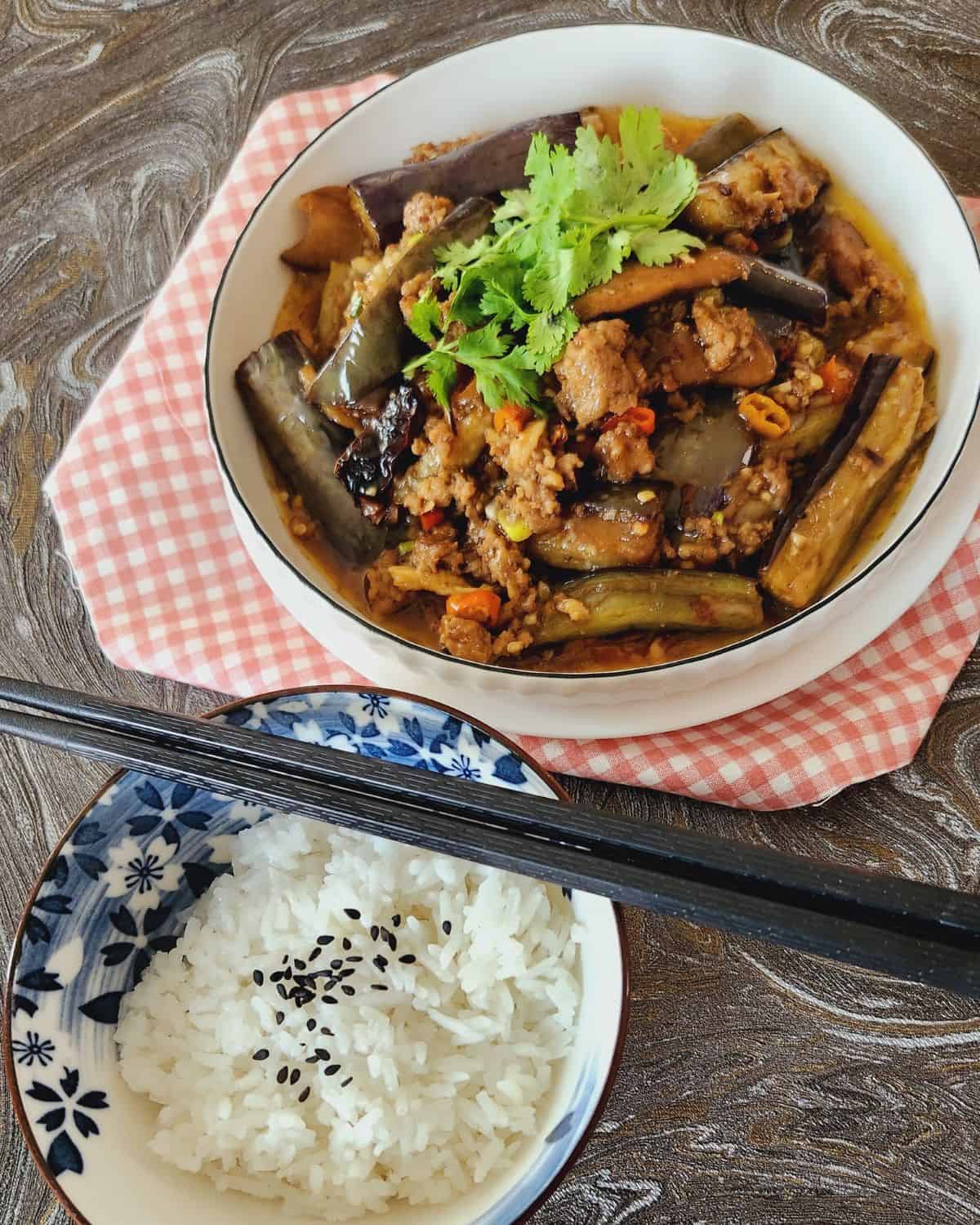 Chinese eggplant stir fry with ground pork in a white plate on pink napkin.
