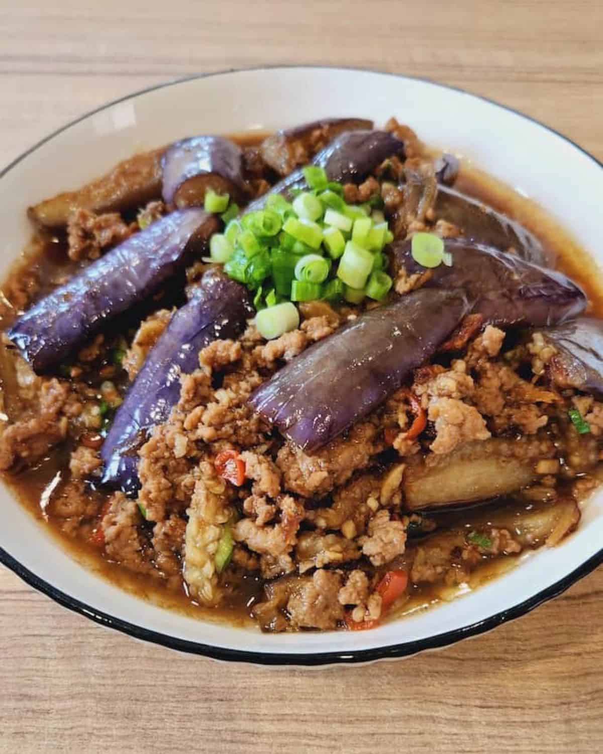 A plate of Chinese eggplant stir fry with ground pork on a wooden table.