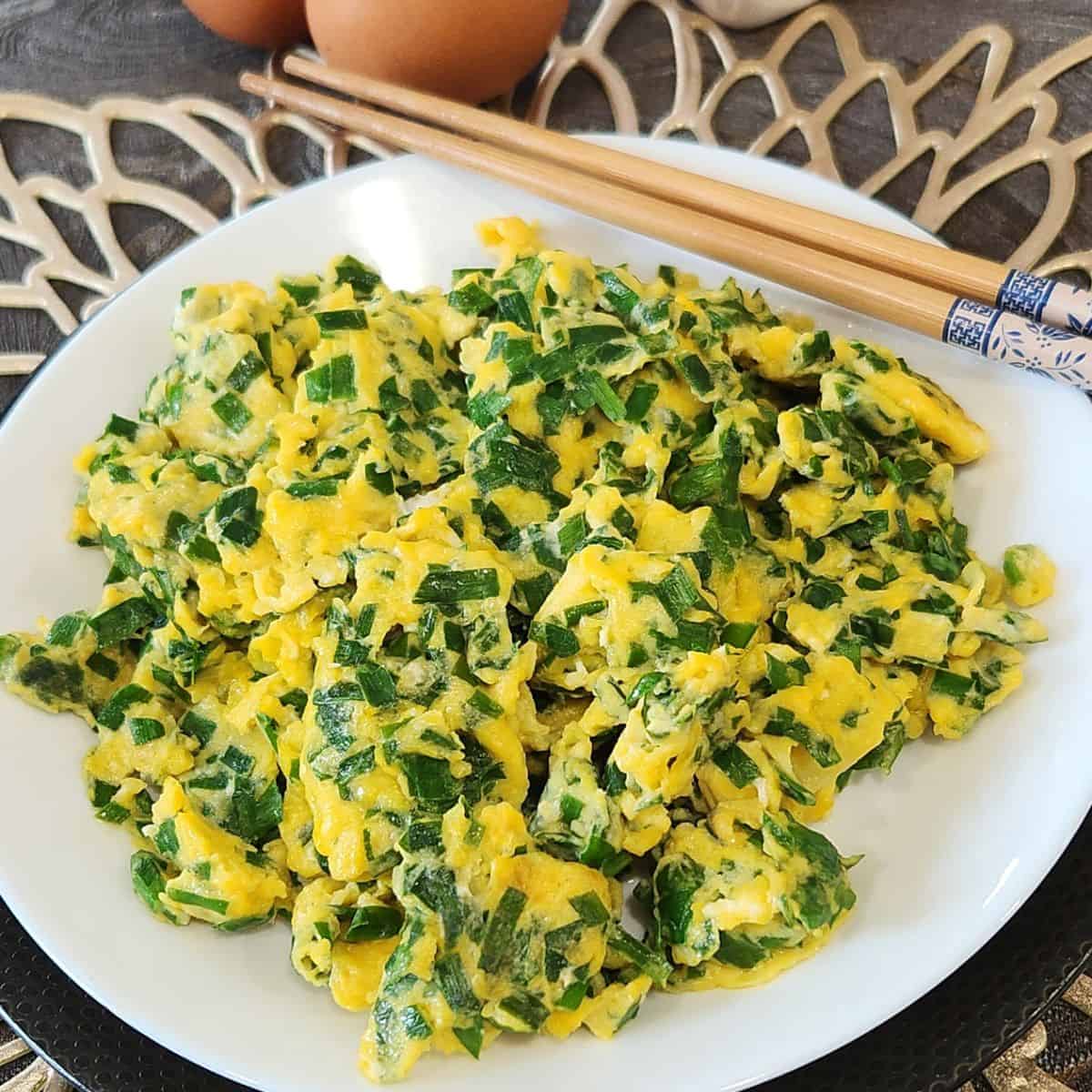 A black plate with Chinese chive eggs on top, garnished with coriander leaves.