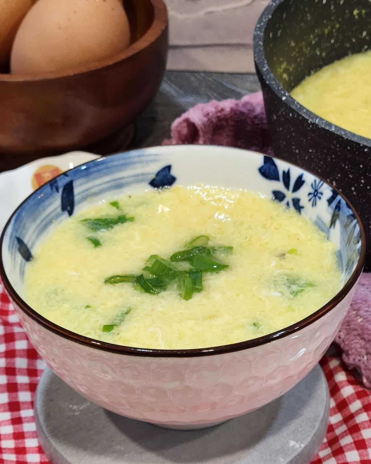A bowl of egg drop soup with green onion in it.