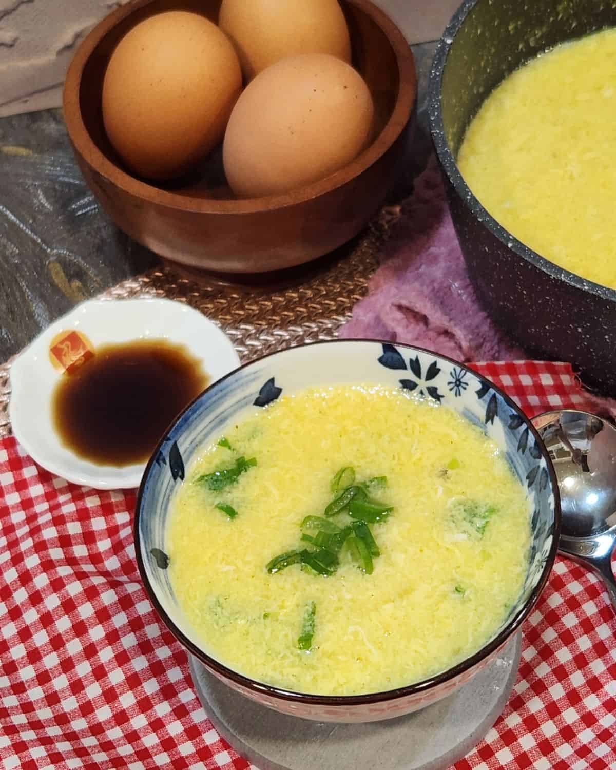 A bowl of egg drop soup with green onion in it.