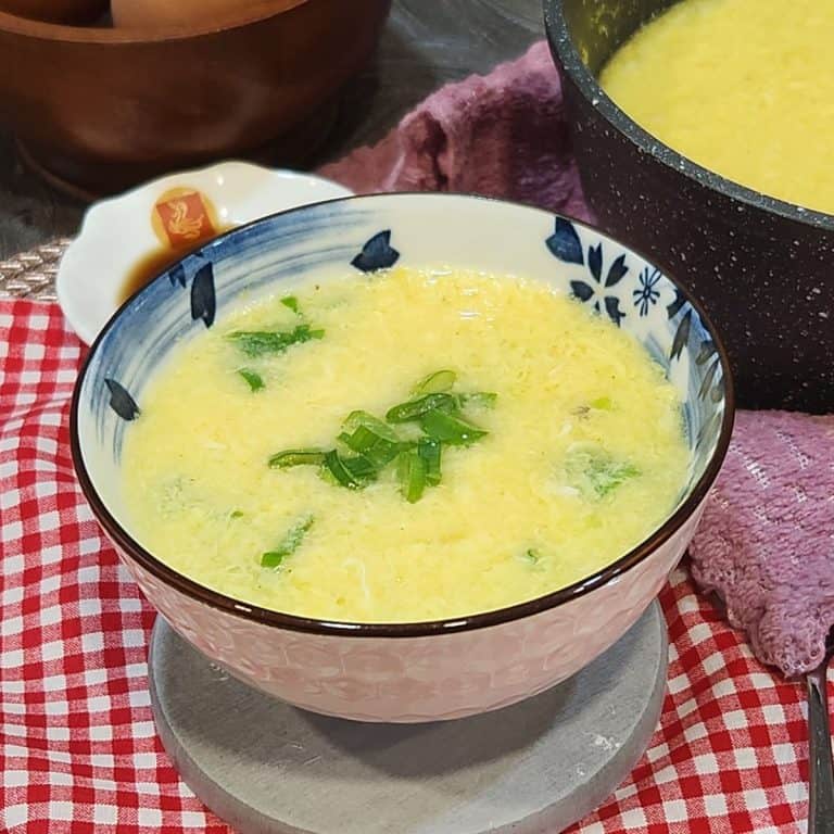 A bowl of egg drop soup with green onion in it.