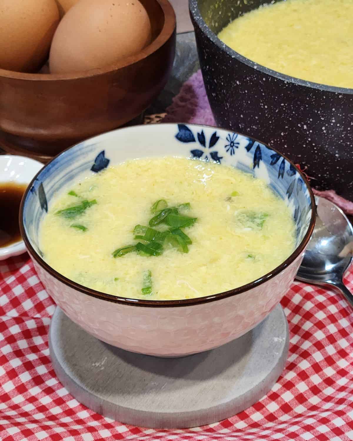A bowl of egg drop soup with green onion in it.
