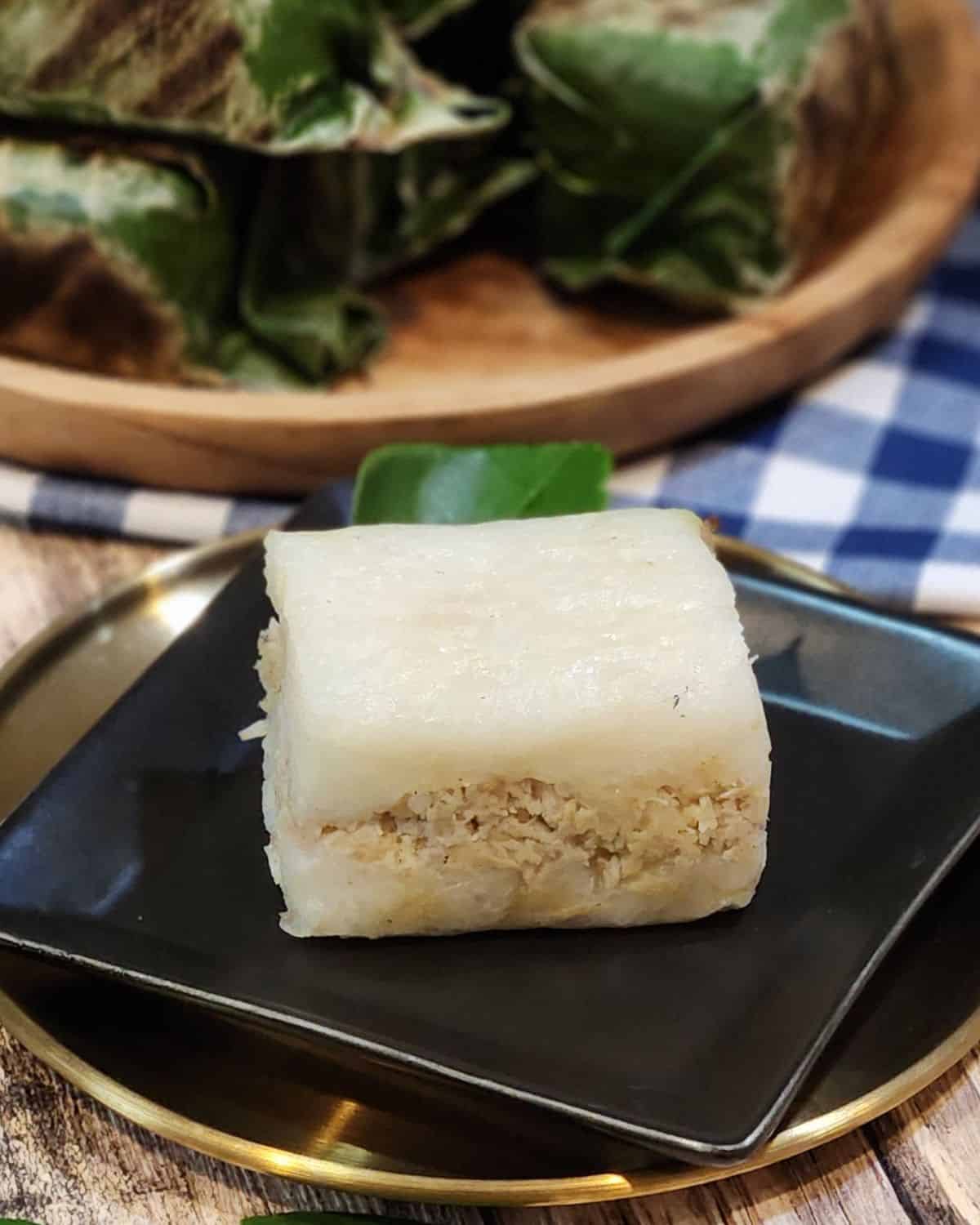 Lemper ayam on a black plate with some wrapped in banana leaves at the back.