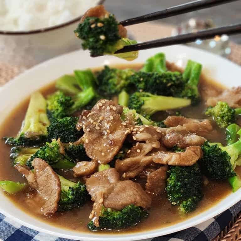 A pair of chopsticks holding pork broccoli stir fry.