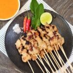 A plate of Sate Taichan with chili, a pinch of salt, and lime wedge.